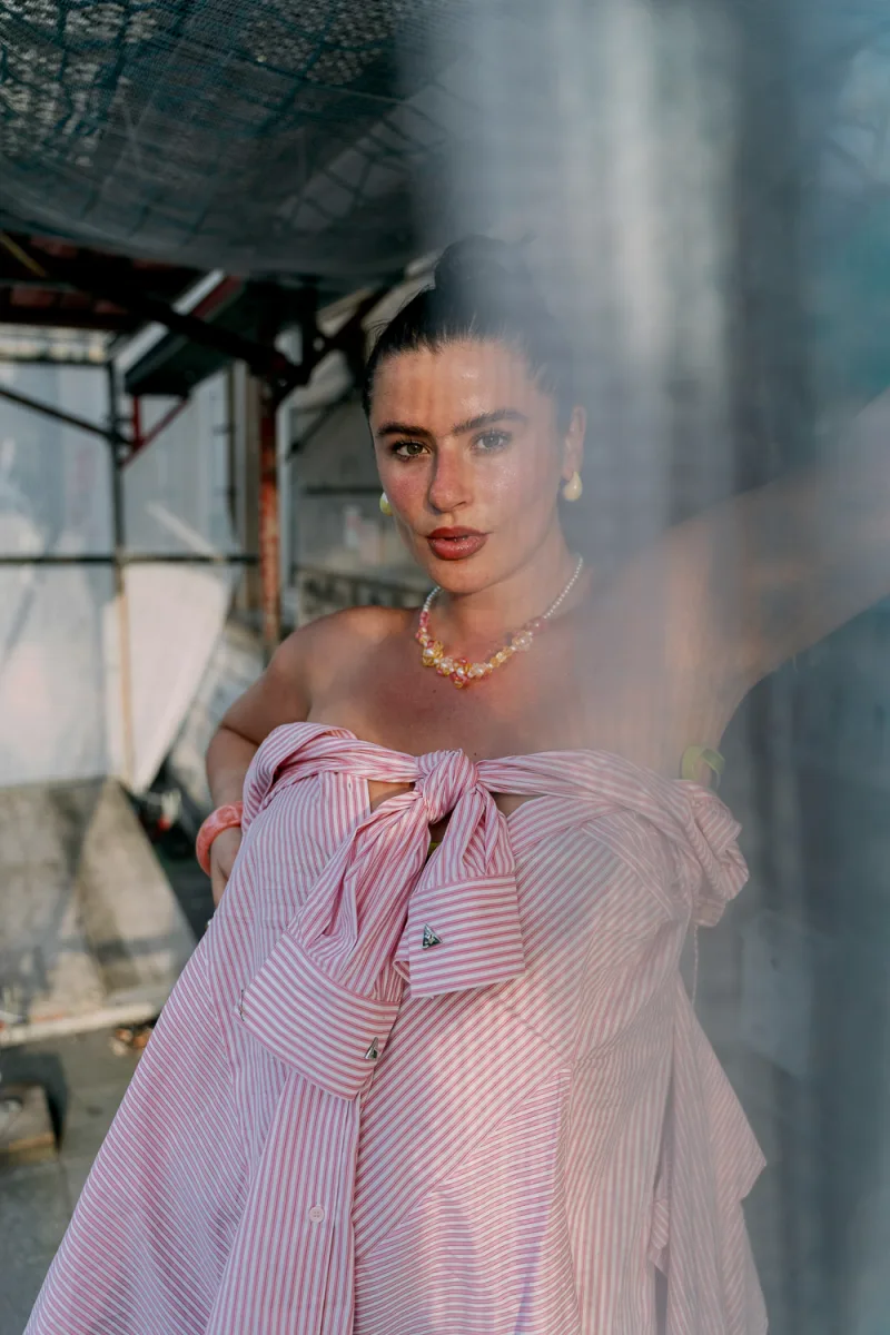Woman in pink striped off-shoulder top with colorful necklace in industrial space