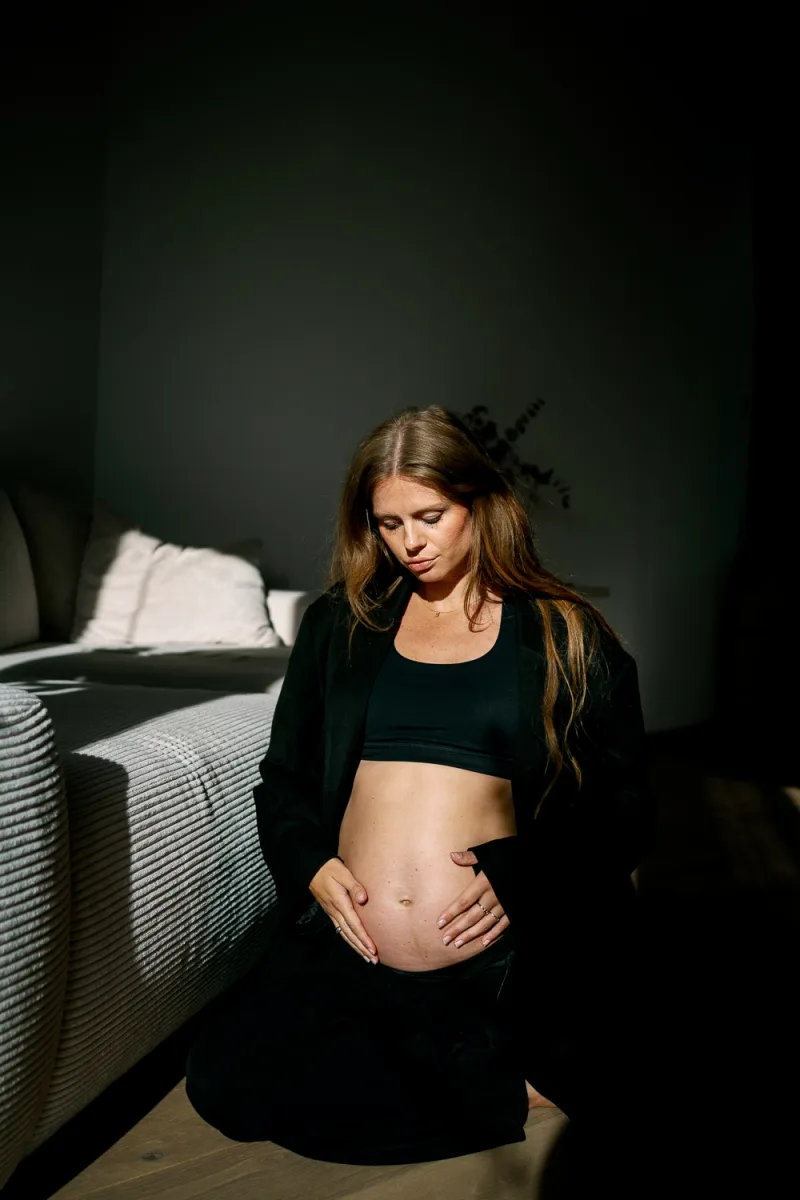 Pregnant woman in black crop top and pants standing in warm amber sunlight