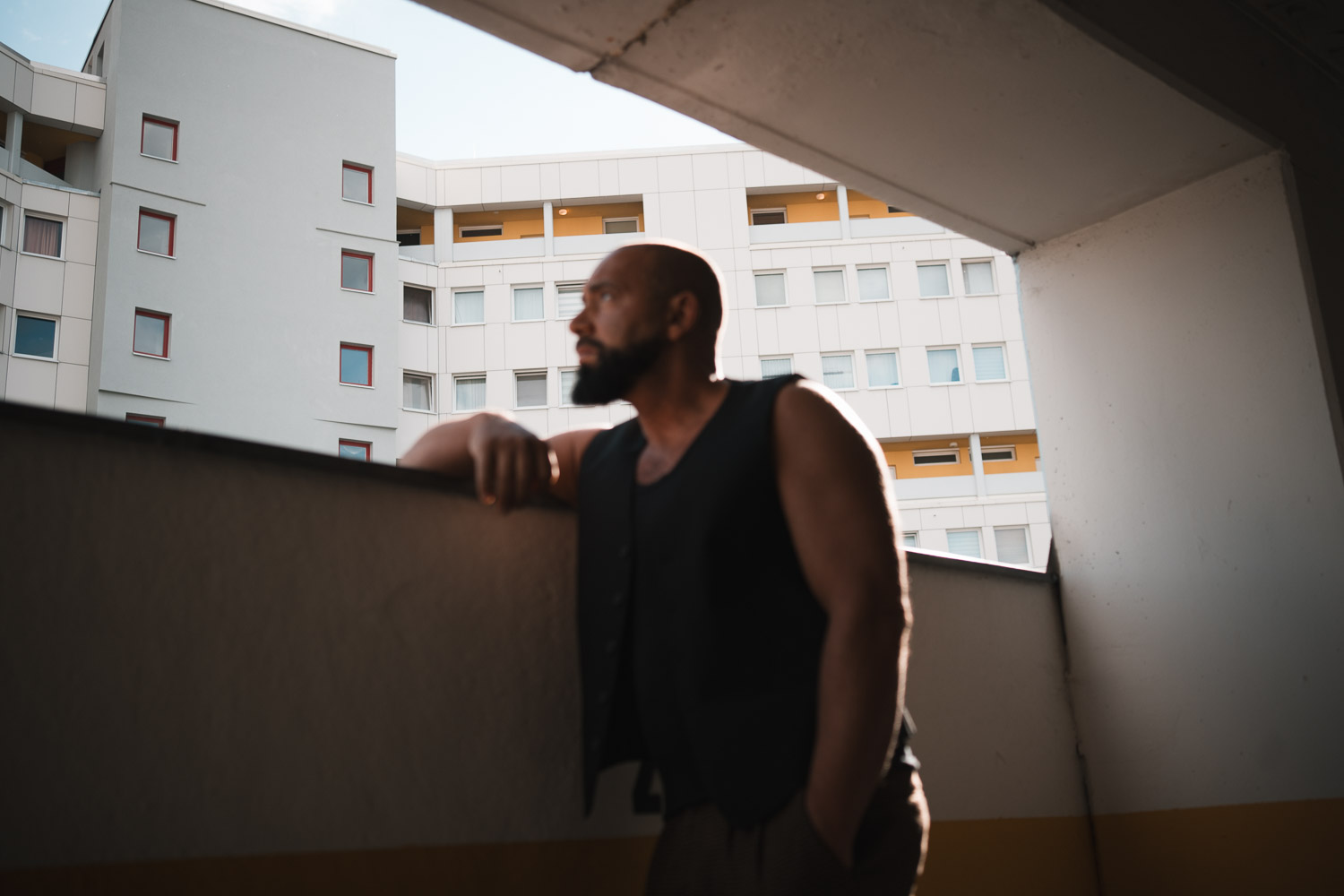 Shirtless man with beard standing against concrete brutalist architecture and sky