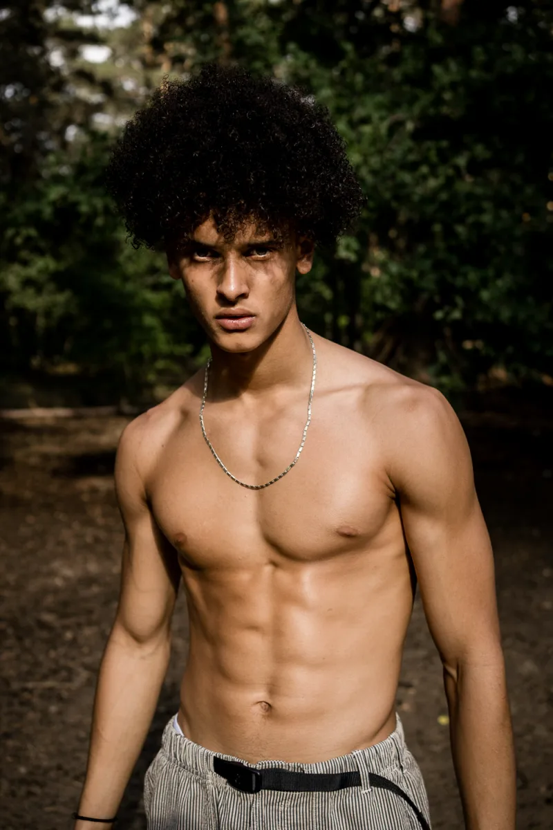 Shirtless young man wearing beaded necklace in natural outdoor greenery setting