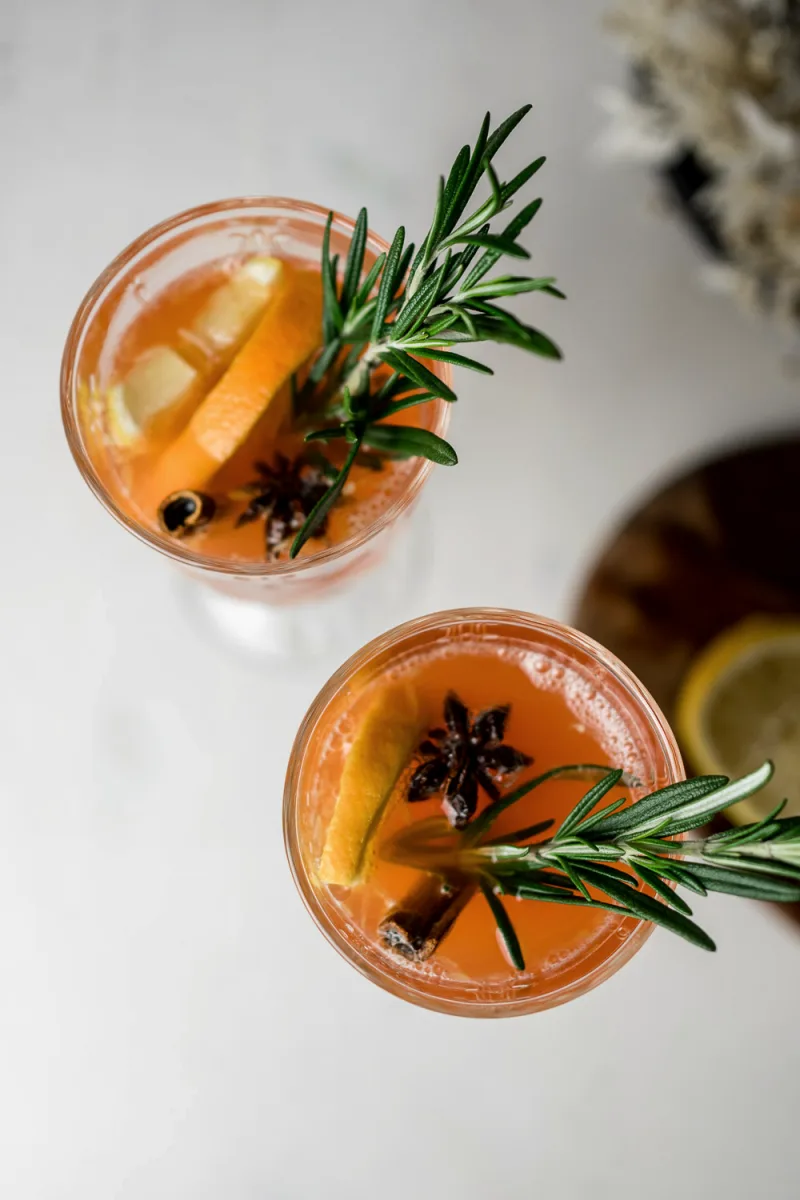 Two amber cocktails with fresh rosemary sprigs and citrus slices overhead view