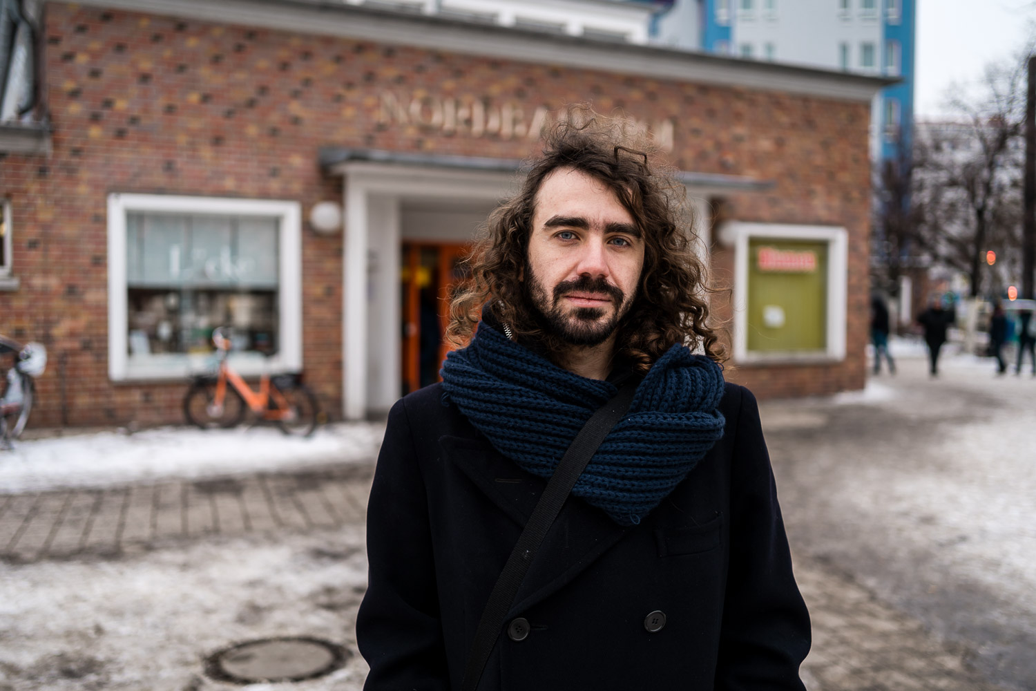 Man with long curly dark hair in elaborate floral button shirt, outdoor portrait pose