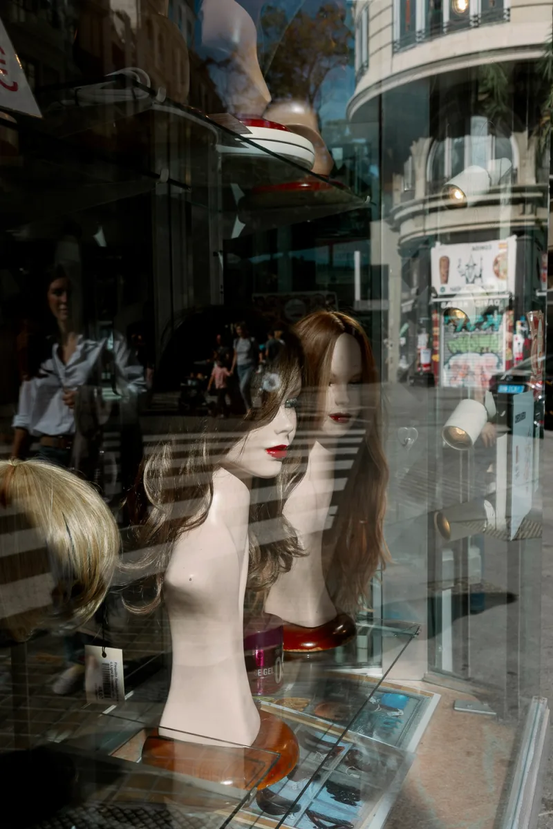 Mannequin heads with long wigs displayed in shop window with street reflections visible