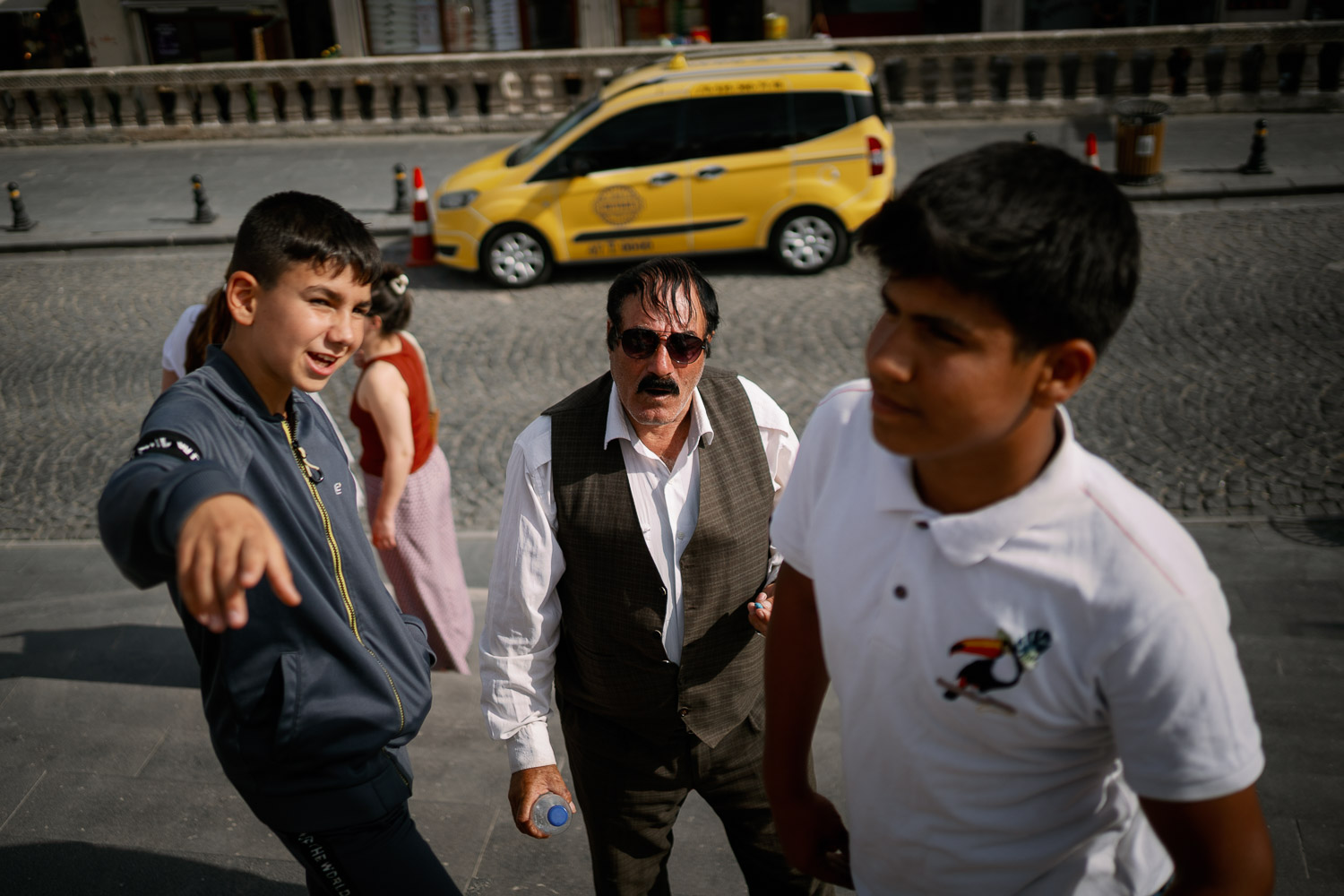 Three men and boy standing together on urban street with yellow taxi behind