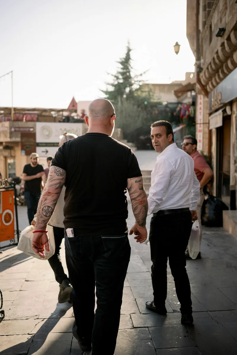 Bald man with arm tattoos walking alongside man in white shirt