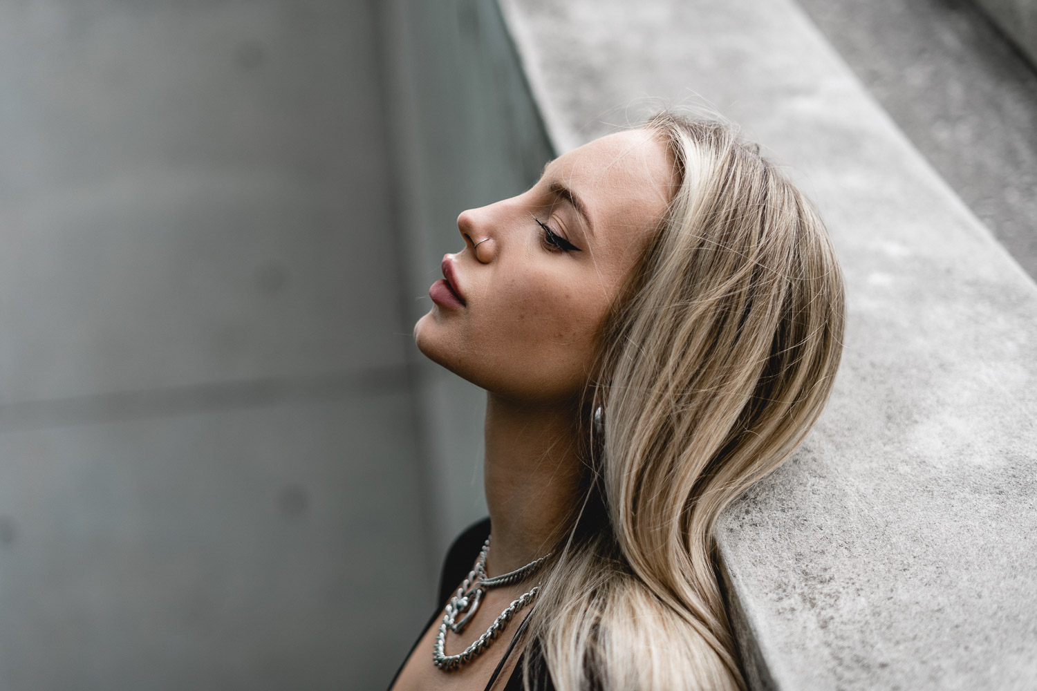 Woman with blonde straight hair and bangs in profile against industrial background