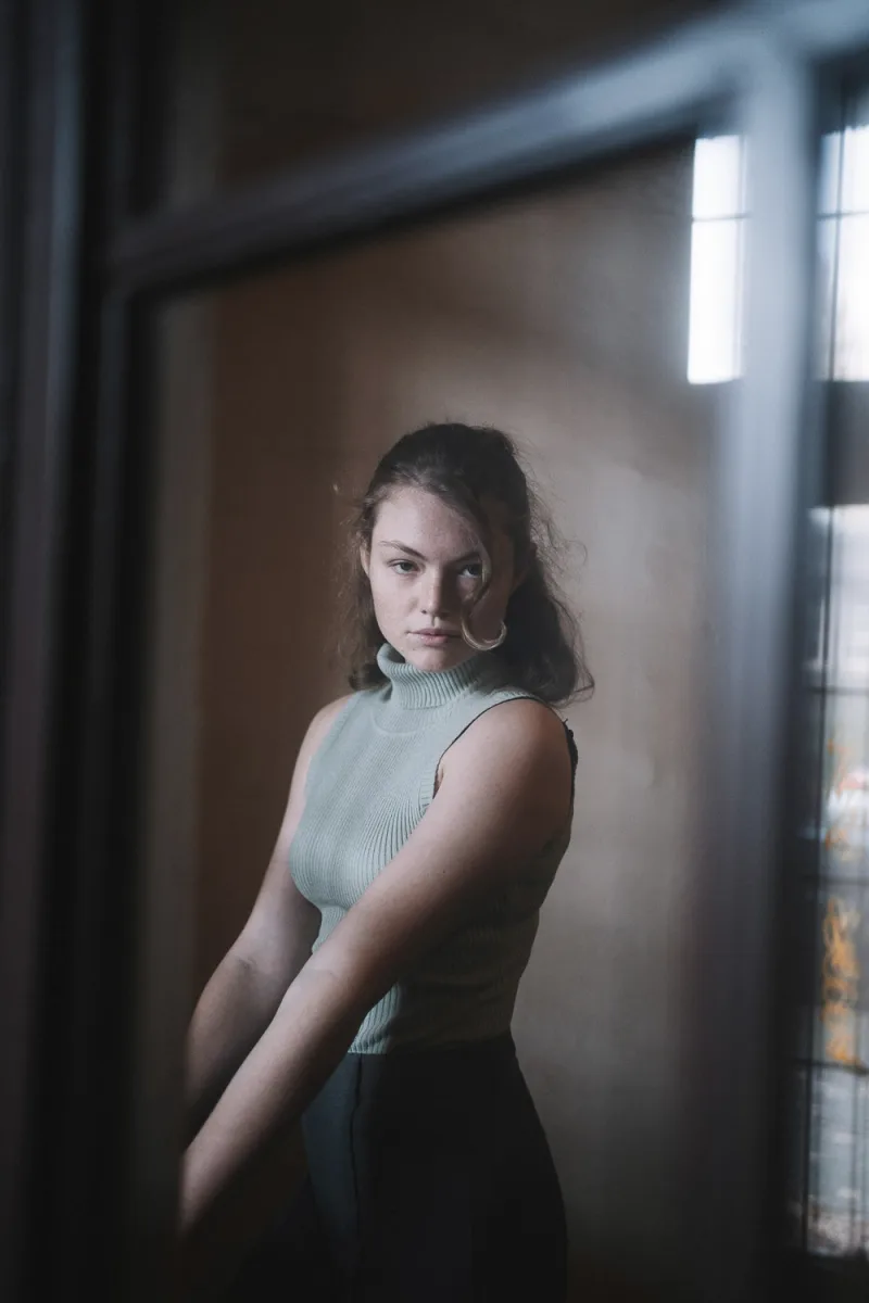 Woman in light ribbed tank top illuminated by window, contemplative side profile