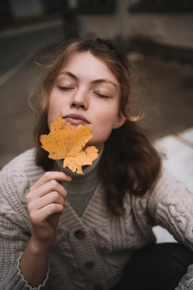 Person with closed eyes holding golden maple leaf up to their face with soft expression