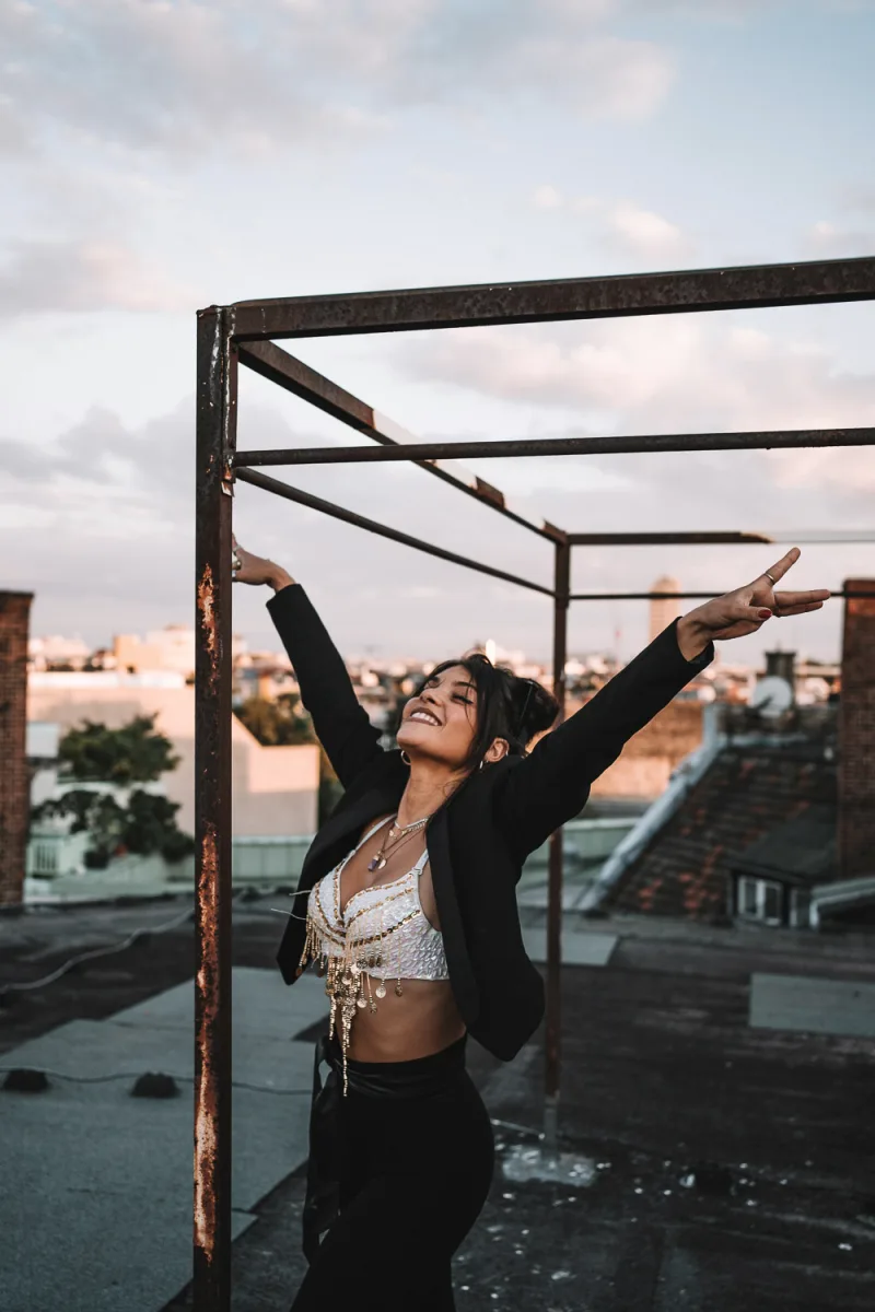 Woman with arms raised joyfully beneath rusted metal frame structure overlooking city